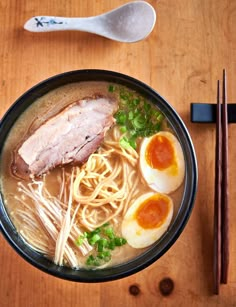 a bowl of ramen with meat, eggs and noodles on a wooden table next to chopsticks