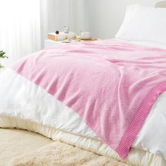 a bed with a pink blanket on top of it next to a white nightstand and window