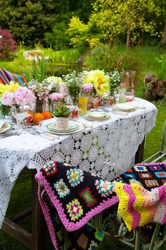 the table is set with crocheted cloths and flowers in vases on it