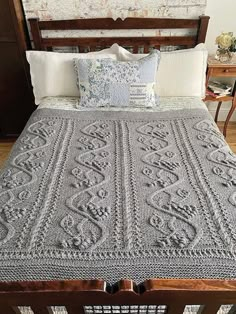 a bed with a gray crocheted blanket on top of it next to a wooden headboard