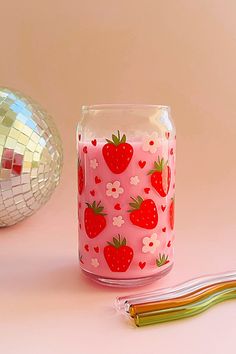 a glass jar with strawberries painted on it next to a toothbrush and disco ball