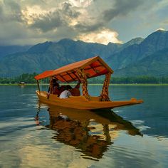 two people in a small boat on the water with mountains in the background and clouds in the sky