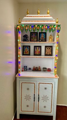 a white cabinet with pictures on the top and lights around it in front of a wall