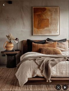 a bed with pillows and blankets on top of it next to a painting hanging above the bed