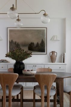 a dining room table with four chairs and a vase on top of it in front of a painting