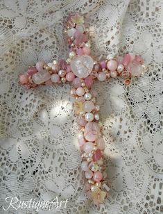 a cross made out of pink and white beads on a lace doily with crochet