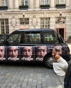 a man talking on his cell phone in front of a car that is painted with images of men's faces