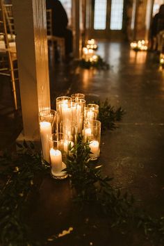 candles are lined up on the floor next to greenery