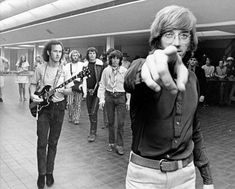 black and white photo of band members in an airport lobby pointing at the camera with one hand