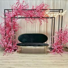 a black couch sitting under a pink flower covered arch in front of a white wall