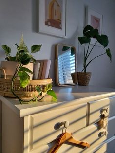 a white dresser with some plants on top of it and a mirror in the background