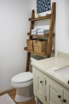 a white toilet sitting next to a bathroom sink under a wooden shelf filled with towels