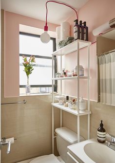 a white toilet sitting next to a bathroom sink under a window in a pink walled room