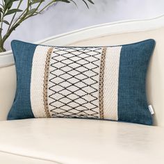 a blue and white pillow sitting on top of a couch next to a potted plant