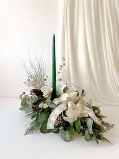 a green candle with white flowers and greenery in front of a white curtained background