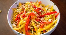 a white bowl filled with yellow and red food on top of a wooden table next to a fork