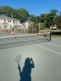 a shadow of a person holding a tennis racquet on a tennis court with houses in the background