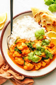 a white plate topped with chicken and rice next to lemon wedges, cilantro