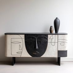 a black and white cabinet with two vases on it's sideboard in front of a wall