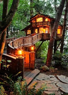 a tree house in the woods with stairs leading up to it's roof and lights on