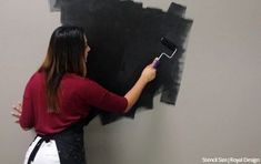 a woman is painting the wall with black paint