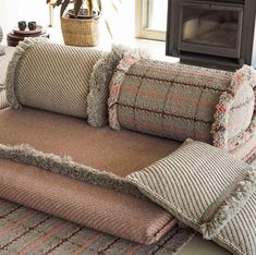 a couch with several pillows on top of it in front of a tv and fireplace