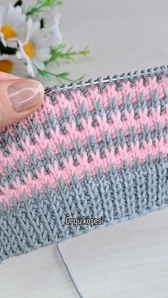 a woman's hand is holding up a knitted wristband with pink and gray stripes