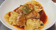 a white bowl filled with dumplings covered in sauce and garnished with herbs