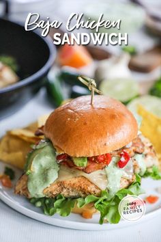 a chicken sandwich with lettuce, tomato and cheese on a plate next to chips