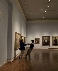 two people standing in an art gallery touching each other's hands with paintings on the wall behind them