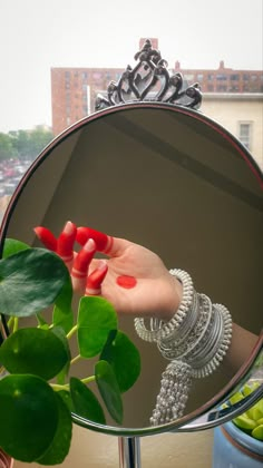 a woman's hand with red nail polish and bracelets is reflected in a round mirror