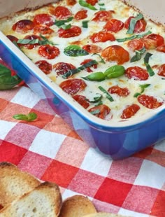 a blue casserole dish with tomatoes and basil on top next to crackers