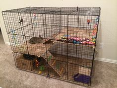 a cage that is filled with toys and other items on the floor in front of a wall