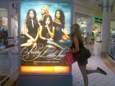 a woman is standing in front of a pretty little lies advertisement at an airport terminal