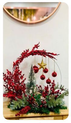 a christmas arrangement with red berries, greenery and baubles in front of a mirror