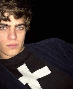 a young man wearing a black and white sweater with a cross on it's chest