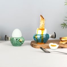 an egg is sitting on a cutting board next to two fish shaped eggs and one has been broken