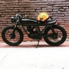 a black motorcycle with a yellow helmet on the back tire and side view mirror, parked in front of a brick wall