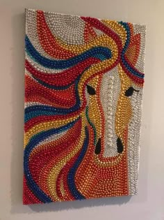 a horse made out of beads is hanging on the wall in front of a white wall