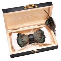 A luxurious feather bow tie with shimmering green and brown tones, neatly placed inside an open wooden box lined with white cushioning.