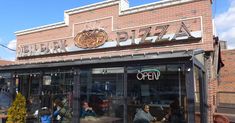 people sitting at tables in front of a pizza shop