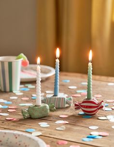 three lit candles sitting on top of a table next to confetti covered plates