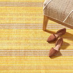 a pair of brown shoes sitting on top of a yellow and white striped rug next to a wooden bench