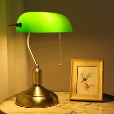 a green lamp sitting on top of a table next to a framed picture and a painting