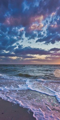 the sun is setting over the ocean with clouds in the sky and waves on the beach