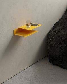 a yellow shelf sitting on the side of a wall next to a black rock with a glass in it