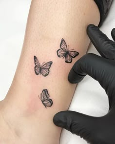 a woman's leg with three butterflies tattooed on the back of her leg, while another person is wearing black gloves