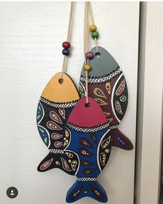 two colorful fish hanging from a hook on a white door with bead necklaces