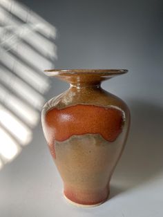 a brown and tan vase sitting on top of a white table next to a window