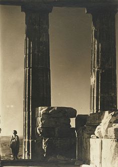 an old black and white photo of two men standing in front of some ruins with columns